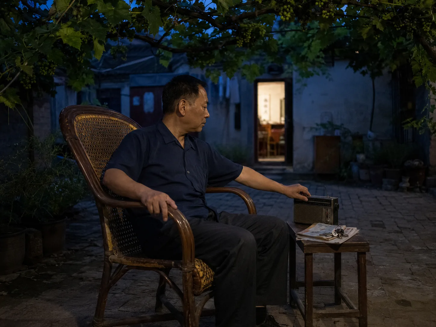 A lane watchman sitting in a woven cane chair beneath a grape arbor at dusk