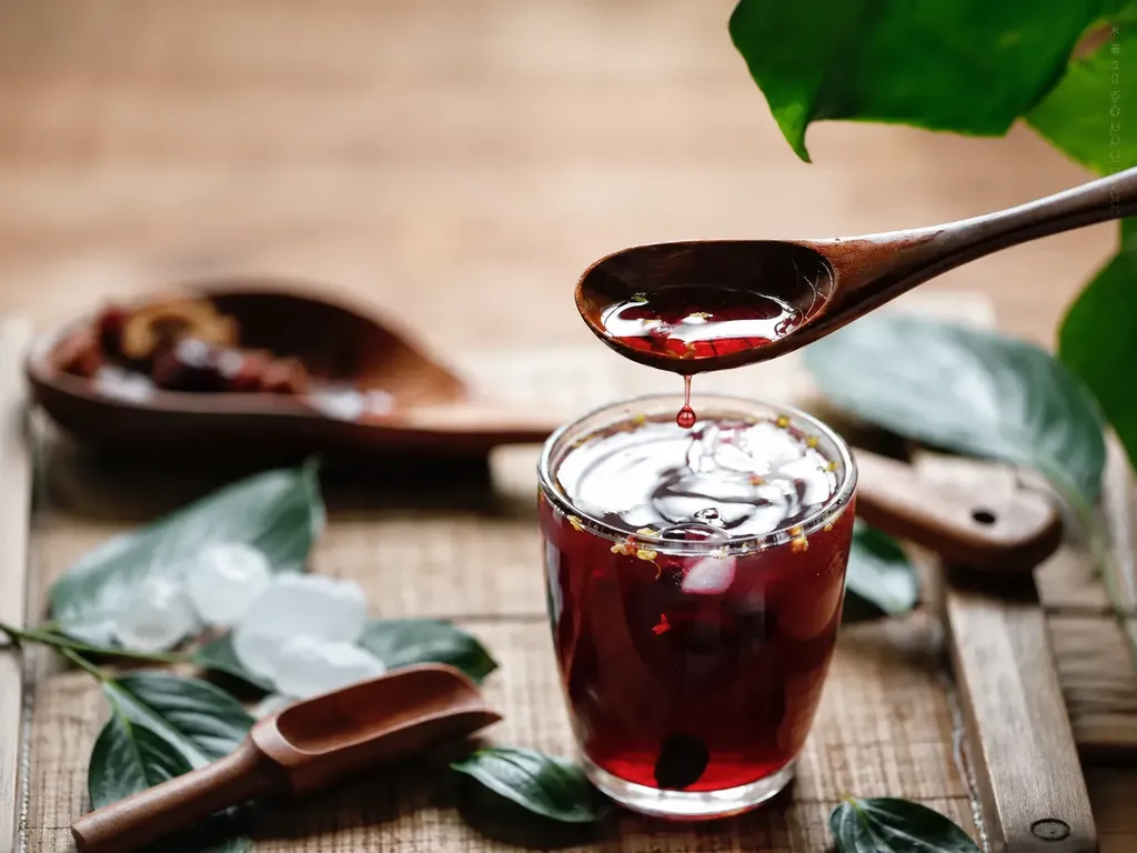 A glass of dark amber sour plum drink beside dried plums